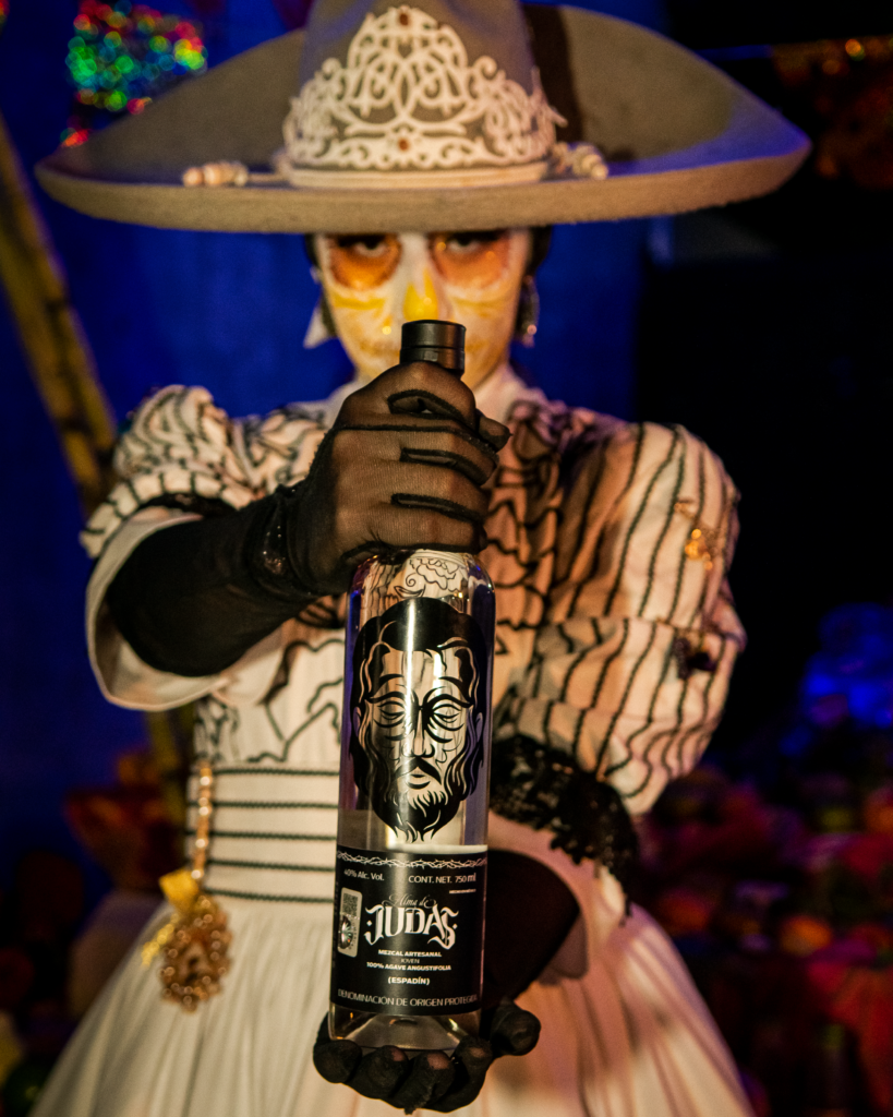 Catrina agarrando con las dos manos y mostrando la botella de Alma de Judas a la cámara