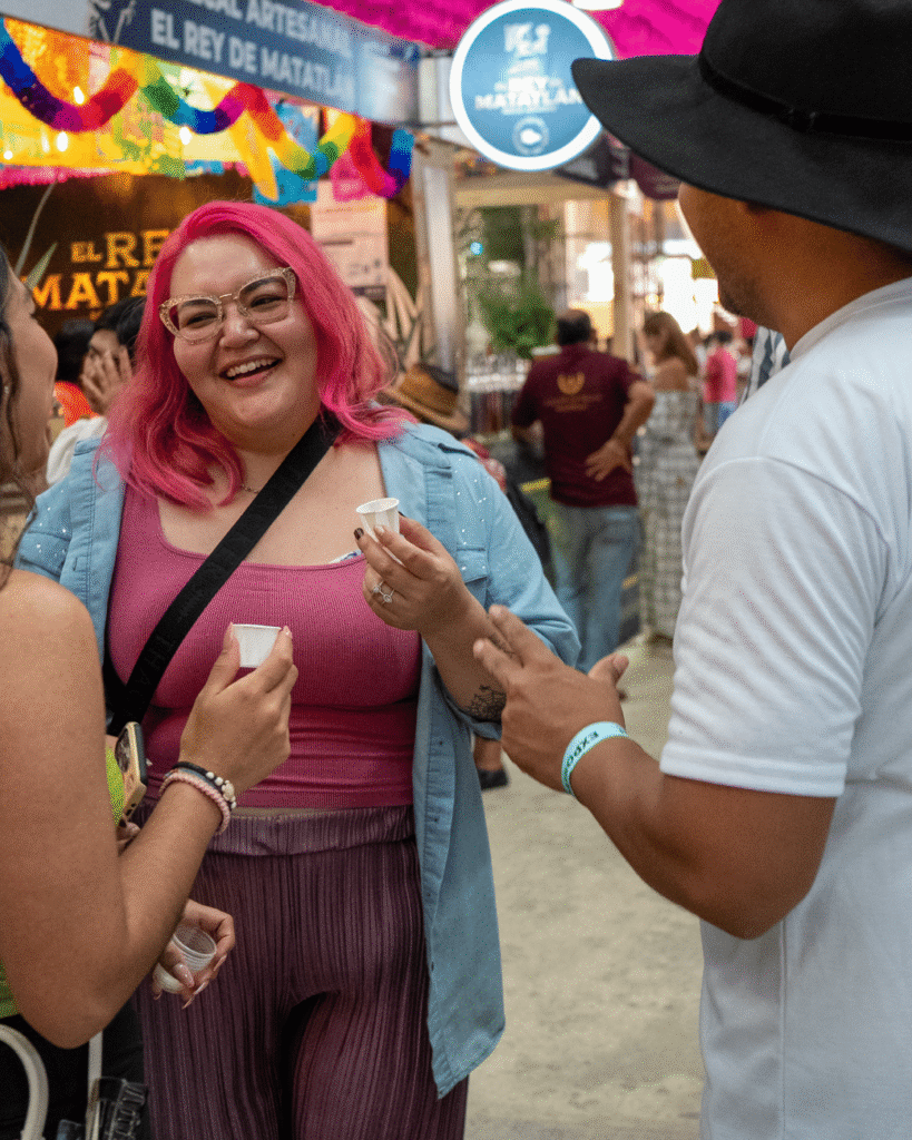 Una chica con el cabello rosa sonriendo con una prueba de mezcal de Alma de Judas en su mano