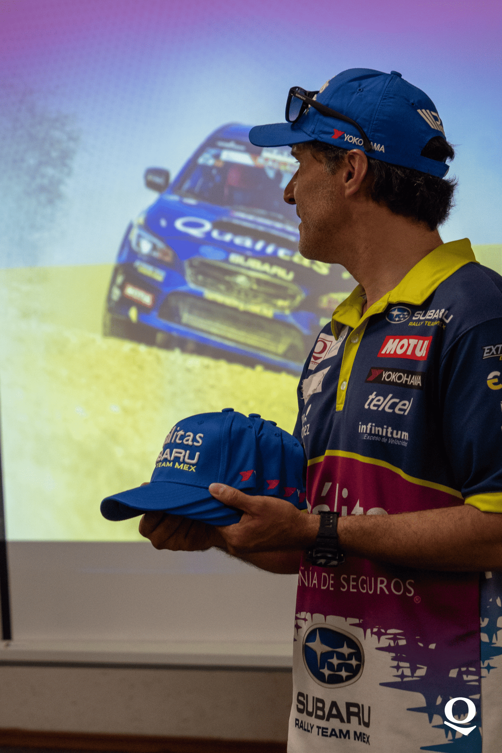 Hombre sosteniendo gorras con un carro de fondo