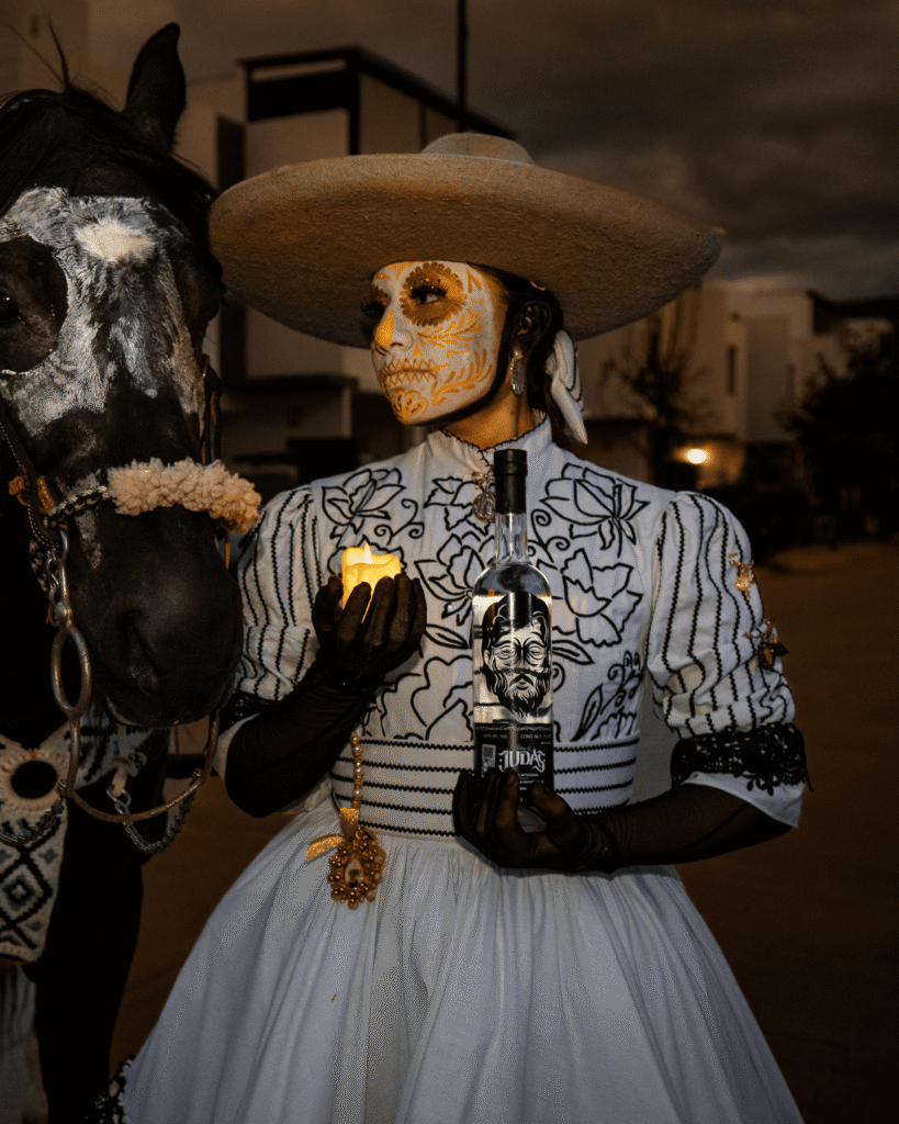 Mujer catrina mirando a su caballo con botella de Alma de Judas en la mano