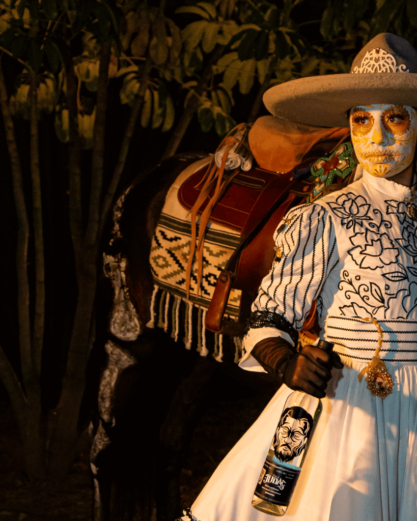 Mujer catrina mirando hacia su derecha con botella de Alma de JUdas y su caballo al lado