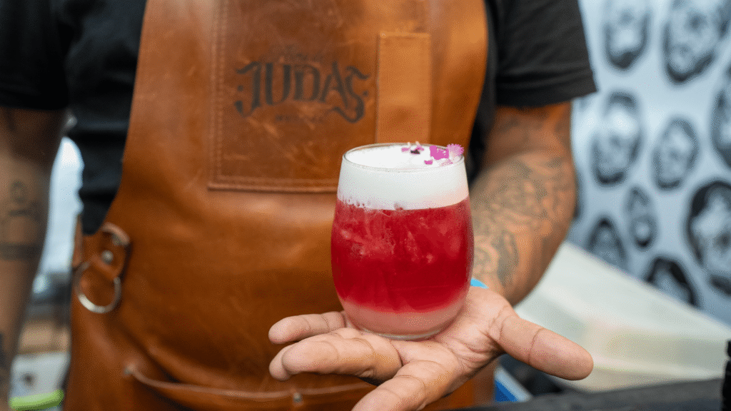 Barman agarrando un coctel preparado color rojo con espuma blanca con su mandil de Alma de Judas